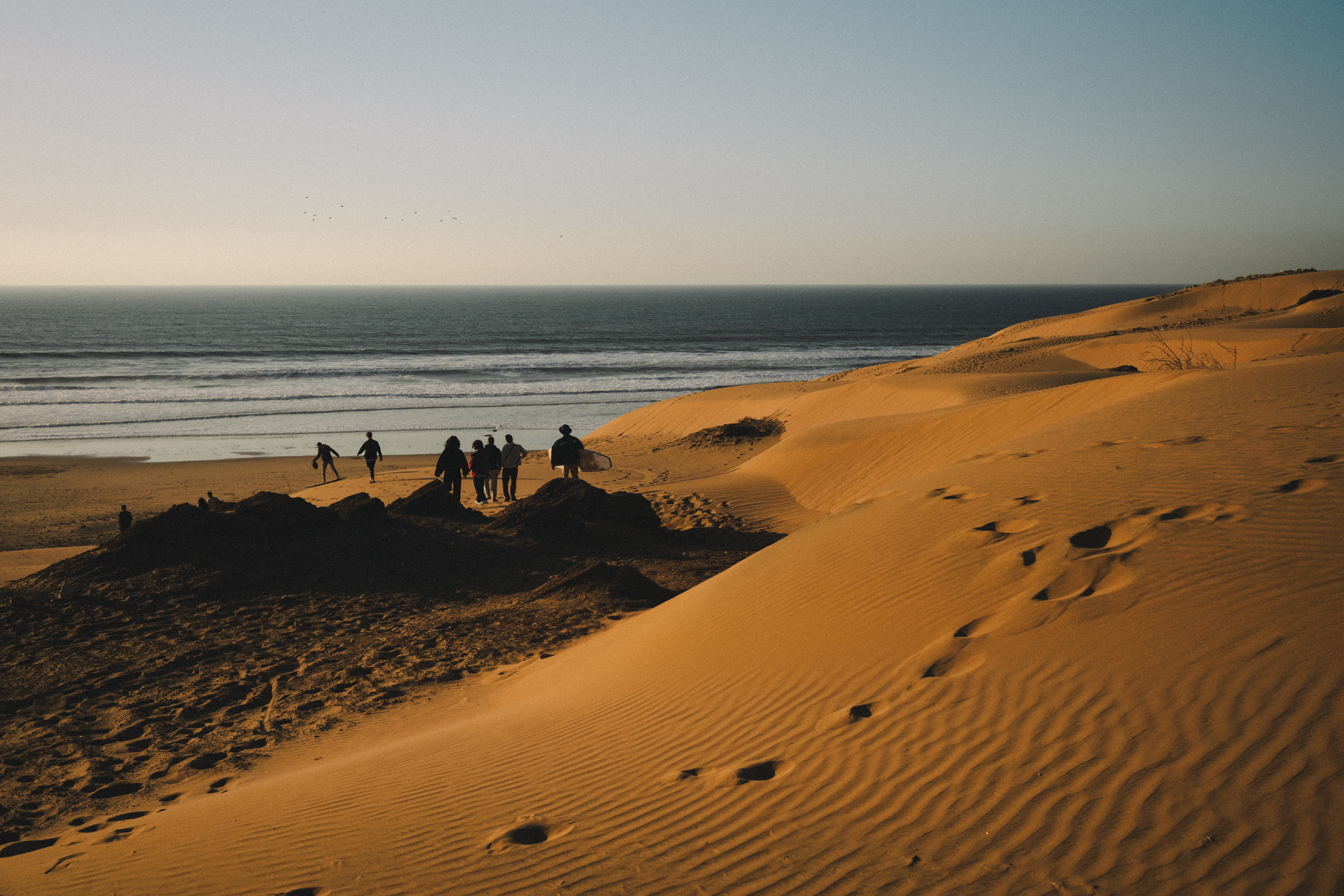 Group of friends around a beach bonfire at sunset with surfboards in the sand